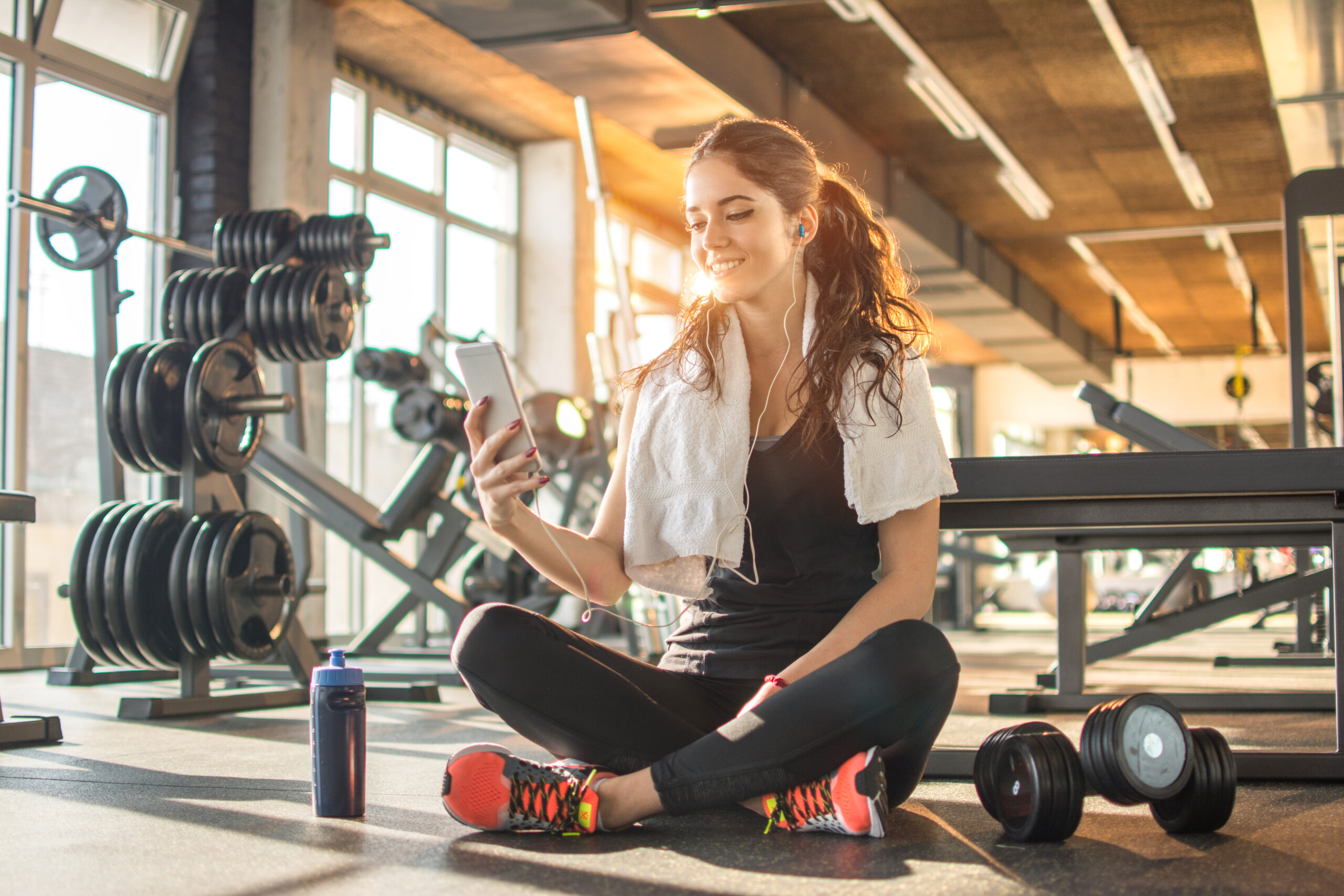 Smiling,Sporty,Girl,With,Earphones,Using,Phone,While,Sitting,Down